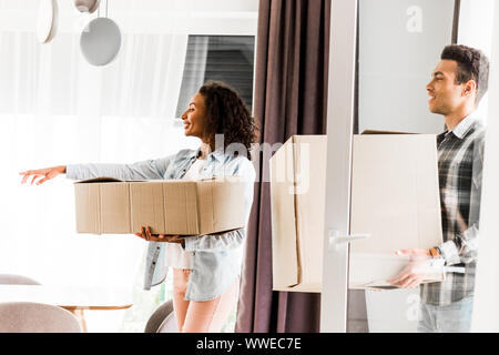 African American mari et femme marche dans chambre et la tenue des boîtes tout en pointant avec la main femme Banque D'Images