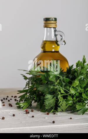 Bouteille d'huile près de la coriandre bung et dispersées de poivre noir et rouge sur la table en bois blanc isolé sur gray Banque D'Images