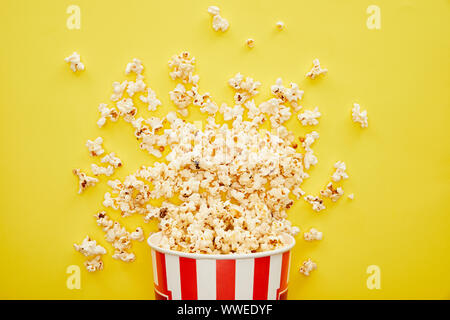 Vue de dessus de délicieux popcorn dispersés de godet sur fond jaune à rayures Banque D'Images