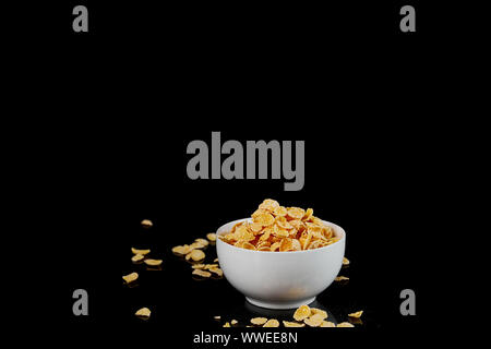 Bol blanc avec cornflakes et morceaux épars isolated on black Banque D'Images