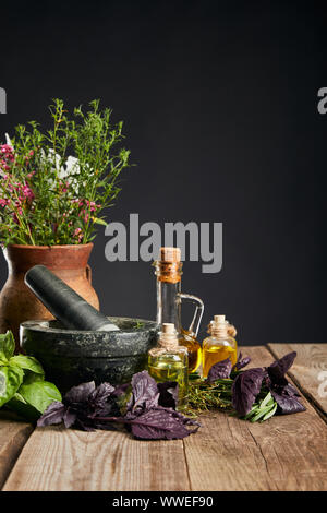 Près de mortier gris vase d'argile avec des herbes sur table en bois isolé sur black Banque D'Images