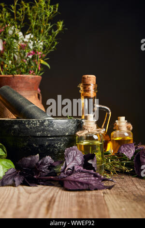 Mortier en pierre près de vase d'argile avec des fleurs sauvages et des herbes sur table en bois isolé sur black Banque D'Images