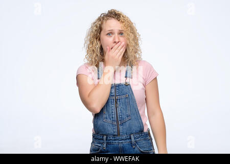 Jeune femme habillée négligemment bouclés couvrant sa bouche de surprise. Studio shot Banque D'Images