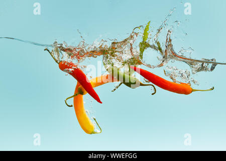 Piments multicolores tomber dans l'eau avec des vagues sur fond bleu Banque D'Images
