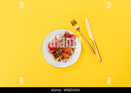 Vue du haut de la plaque avec gaufre savoureuse et des fraises pour le petit-déjeuner sur jaune Banque D'Images