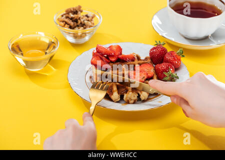 Portrait de femme près de la plaque sur les gaufres de coupe bol et tasse de thé sur fond jaune Banque D'Images