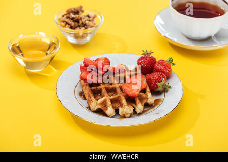 Petit-déjeuner servi avec waffle et fraises à plaqué, miel, noix et d'un plateau sur fond jaune Banque D'Images