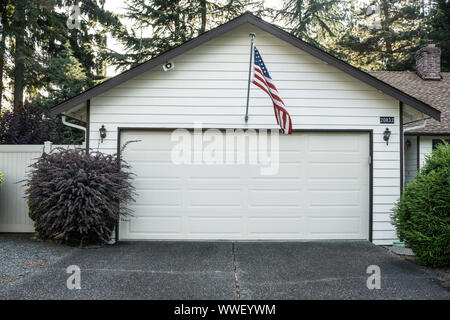 Garage de banlieue blanc garniture avec parement de bois horizontal bordé de brun foncé avec drapeau américain centré au-dessus de la porte en agitant une légère brise Banque D'Images