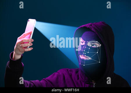 Masque féminin hacker en holding smartphone protégé avec système de reconnaissance faciale Banque D'Images