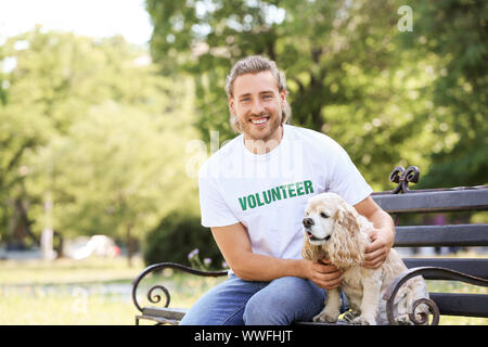 Des bénévoles masculins avec mignon chien assis sur un banc à l'extérieur Banque D'Images