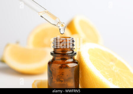 Des gouttes d'huile essentielle d'agrumes pipetter dans bouteille sur fond blanc Banque D'Images