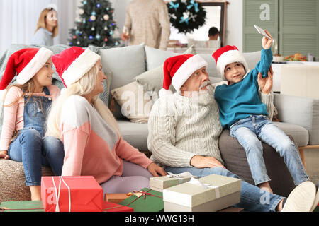 Heureux grands-parents et petits enfants à Santa Claus hats en tenant à la maison selfies Banque D'Images