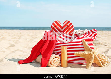 Sac avec des tongs, maillot de bain, serviette et cosmétiques sur plage de sable fin Banque D'Images