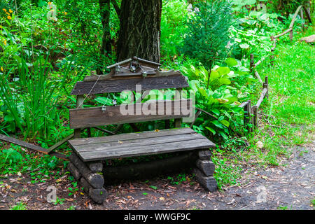 Un vieux banc en bois dans le parc entre les arbres et l'herbe verte dans la forêt le long de laquelle il y a un chemin pour marcher. Reste et la tranquillité dans l'un frais Banque D'Images