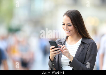 Heureux femme contrôle smart phone en ligne permanent contenu dans la rue Banque D'Images