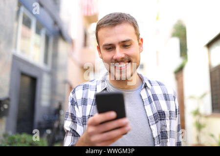 Vue avant portrait of a happy guy à l'aide de smart phone à marcher vers vous dans la rue Banque D'Images