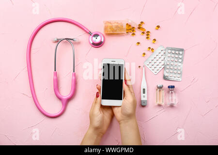 Mains de médecin avec téléphone mobile moderne, stéthoscope et comprimés sur un fond de couleur Banque D'Images