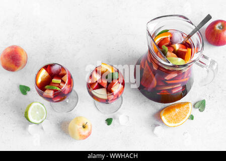 Vin rouge sangria ou punch aux fruits et de la glace dans les verres et pichet. Des fruits rafraîchissante sangria sur fond blanc, copie de l'espace. Banque D'Images