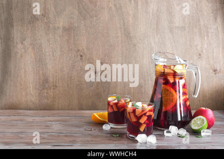 Vin rouge sangria ou punch aux fruits et de la glace dans les verres et pince. Des fruits rafraîchissante sangria sur fond de bois, copie de l'espace. Banque D'Images