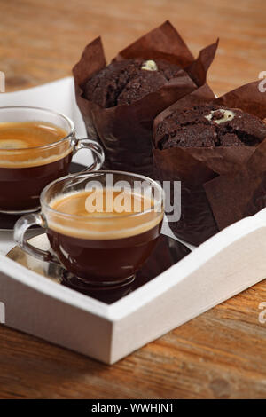 Photo de deux muffins de chocolat et deux tasses de café espresso ou café reposant sur un bac blanc au service de profondeur de champ à l'accent au milieu Banque D'Images