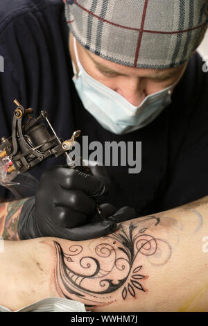 Un tatoueur d'appliquer son art sur la jambe d'une femme. Biens fournie inclut des tatoueurs artwork. Banque D'Images