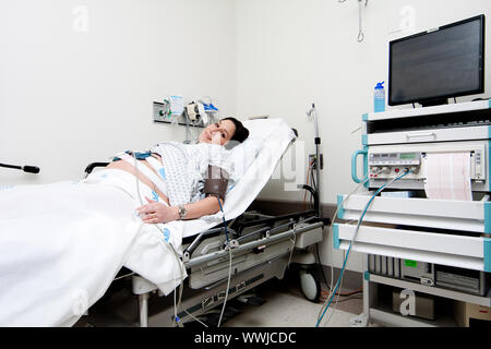 Caucase enceintes Hispanic Latina woman laying in a hospital gurney lit dans l'unité de triage médical faire un test de réactivité fœtale (NST) tout en étant accroché u Banque D'Images