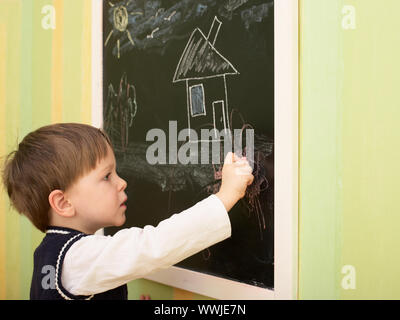 3 ans garçon mignon attire l'house on blackboard Banque D'Images