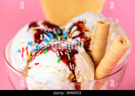 Boules de crème glacée dans un bol en verre avec une sauce au chocolat, cookies et sprinkles jonchaient sur fond rose, Close up Banque D'Images