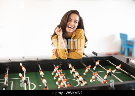 Young happy brunette woman playing table football pendant les pauses au bureau Banque D'Images