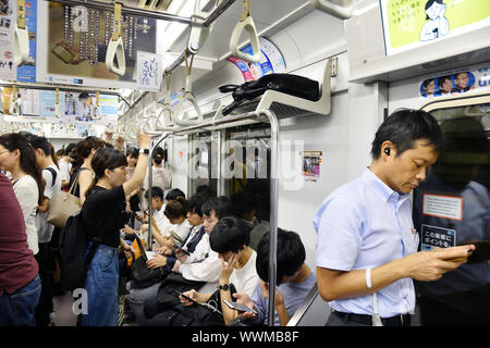 un wagon de train de banlieue bondé au Japon, où plusieurs passagers sont assis et debout tout en regardant leurs smartphones - Tokyo - Japon Banque D'Images