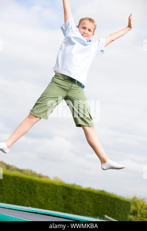 Jeune garçon sautant sur trampoline smiling Banque D'Images