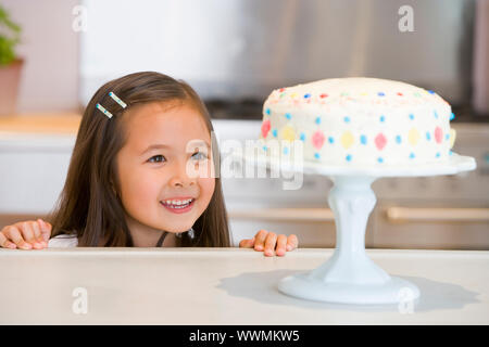 Jeune fille au comptoir de la cuisine à la recherche au gâteau smiling Banque D'Images