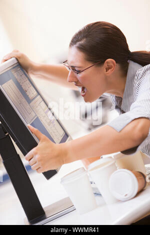 Woman in computer room saisissant son moniteur et crier Banque D'Images