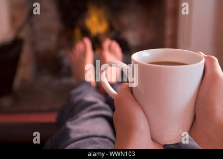 Pieds de réchauffement climatique à la cheminée avec des mains tenant le café Banque D'Images