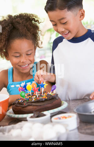 Deux enfants en cuisine avec gâteau d'anniversaire, smiling Banque D'Images