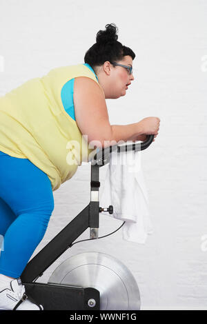 L'excès de Woman Riding Exercise Bike Banque D'Images