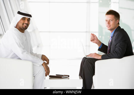 Deux hommes d'affaires à l'intérieur avec un ordinateur portable talking and smiling Banque D'Images