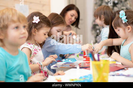 Groupe d'enfants sur place arts leçon en maternelle. Les mains de l'enseignant aide les enfants à travailler. Activités en classe les élèves de maternelle Banque D'Images