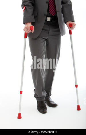 La partie inférieure du corps d'une mobilité ou blessés businessman walking sur une paire de béquilles, studio sur blanc Banque D'Images