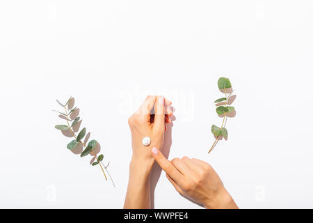 Woman's hands appliquer crème cosmétique à côté de branches d'eucalyptus sur tableau blanc, télévision jeter arrangement. Banque D'Images