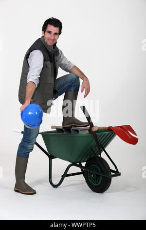 Travailleur de la construction montrant outre de son casque, une brouette et outils Banque D'Images