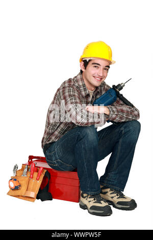 Jeune artisan holding a drill et assis sur une boîte à outils Banque D'Images