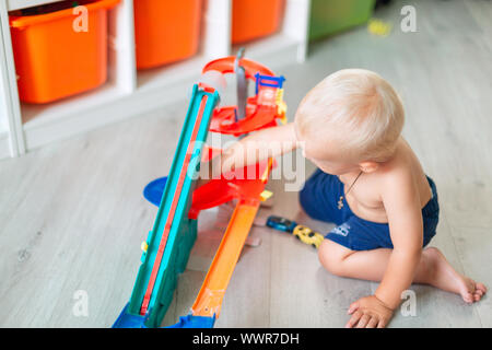 Cute baby boy playing with toy cars sur la bonne voie dans la chambre d'enfant Banque D'Images