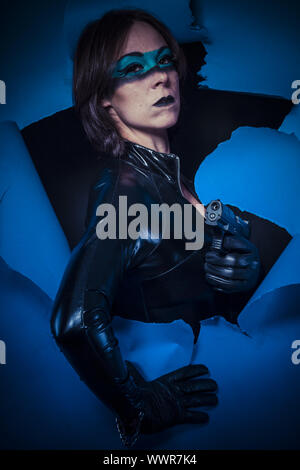 Pistolet, brune en latex costume noir, pistolet sur papier cassé Banque D'Images