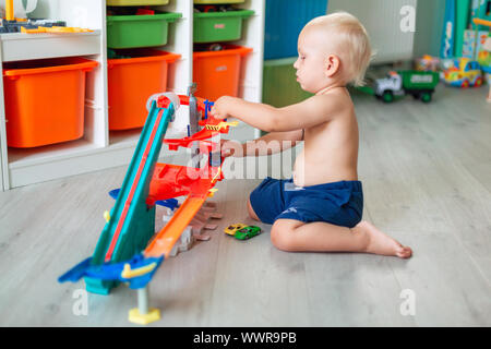 Cute baby boy playing with toy cars sur la bonne voie dans la chambre d'enfant Banque D'Images