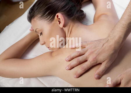 Massage et relaxation, beautiful brunette woman détente sur une civière, recevant un massage thérapeutique de mains d'une professe Banque D'Images