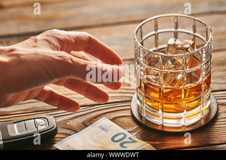 La main de l'homme atteindre au verre avec de l'alcool boire et clé de voiture. Boire et conduire concept. Banque D'Images