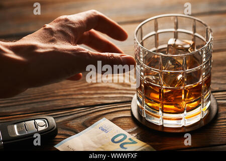 La main de l'homme atteindre au verre avec de l'alcool boire et clé de voiture. Boire et conduire concept. Banque D'Images