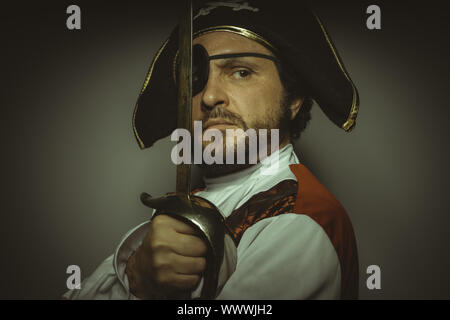 Homme avec barbe, habillé comme un pirate, avec cache-oeil et épée en acier Banque D'Images