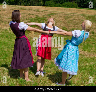 Trois filles habillées en dirndl colorée dansant sur un pré Banque D'Images